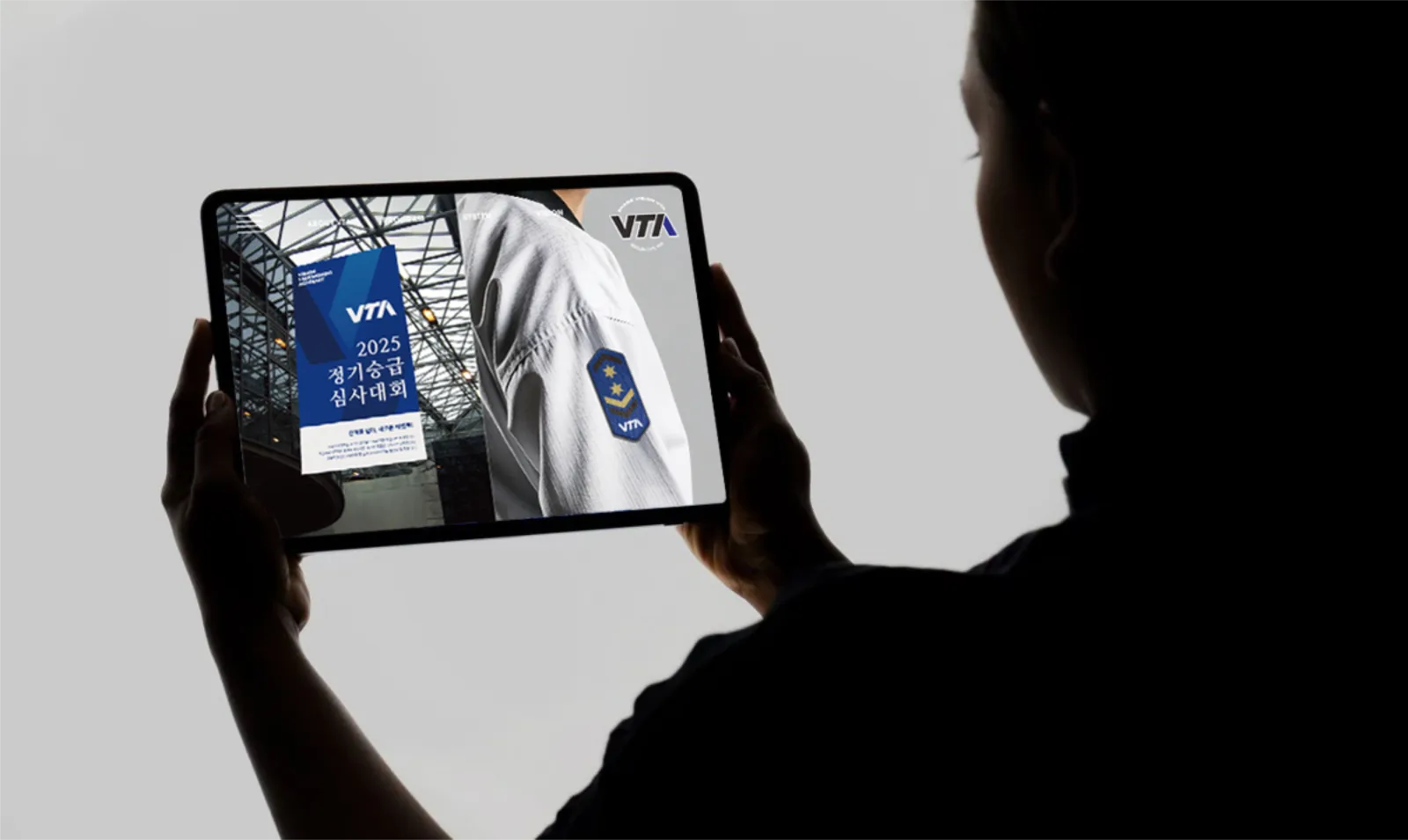 태블릿 화면에 VTA 로고, 수련복과 정기 승급 심사 안내를 보여주는 브랜드 연출 이미지