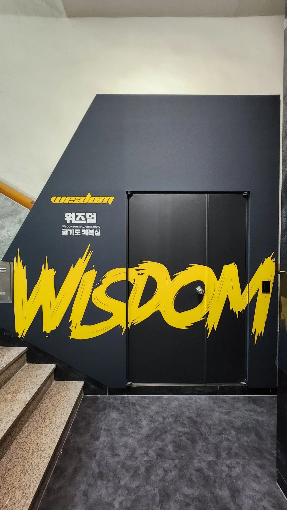 블랙 벽면과 옐로 WISDOM 그래픽이 적용된 체육관 입구